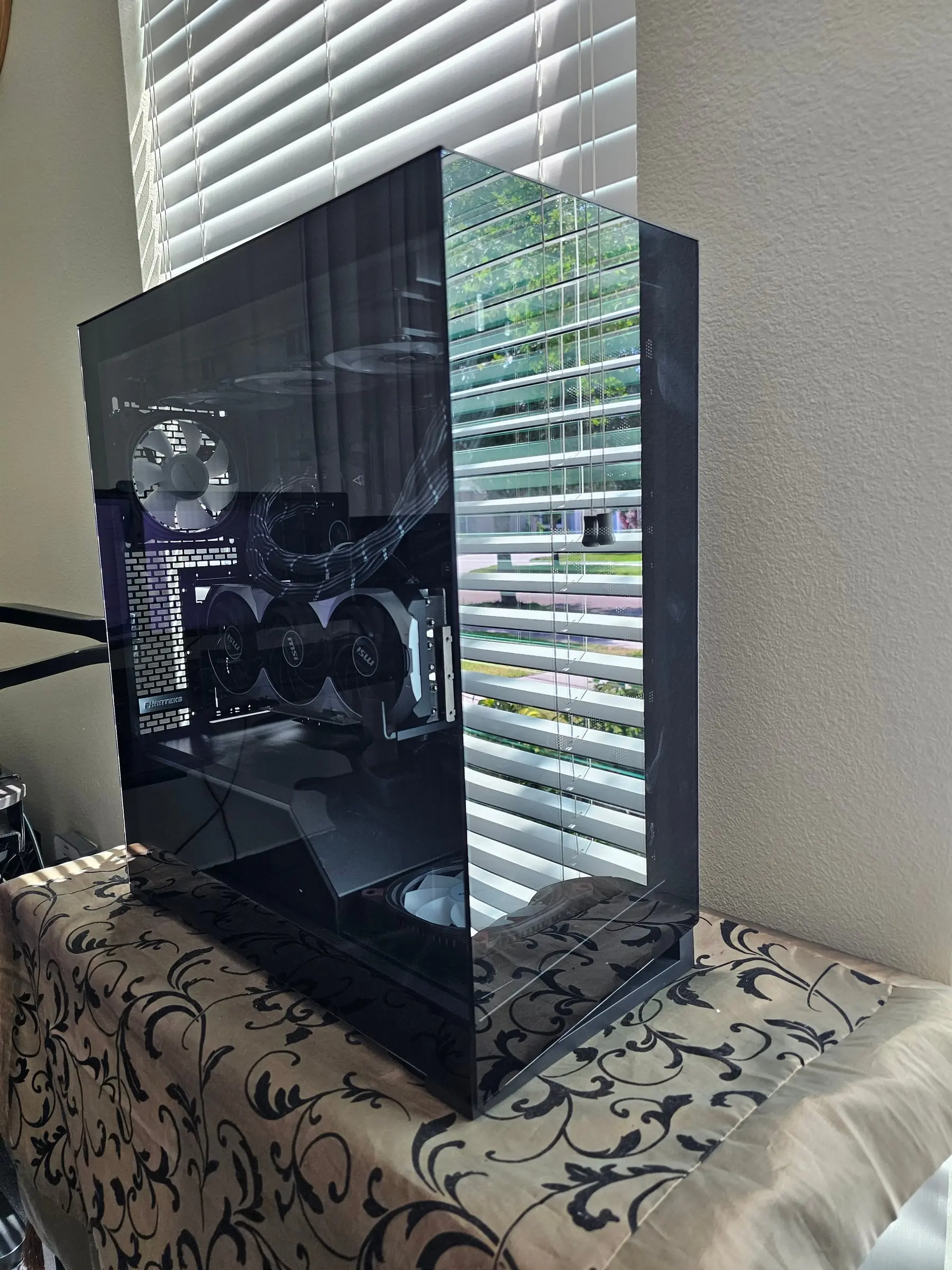 All-black NV5 unpowered in daylight, triple-fan RTX 5070 Ti and sleeved cables behind smoked glass
