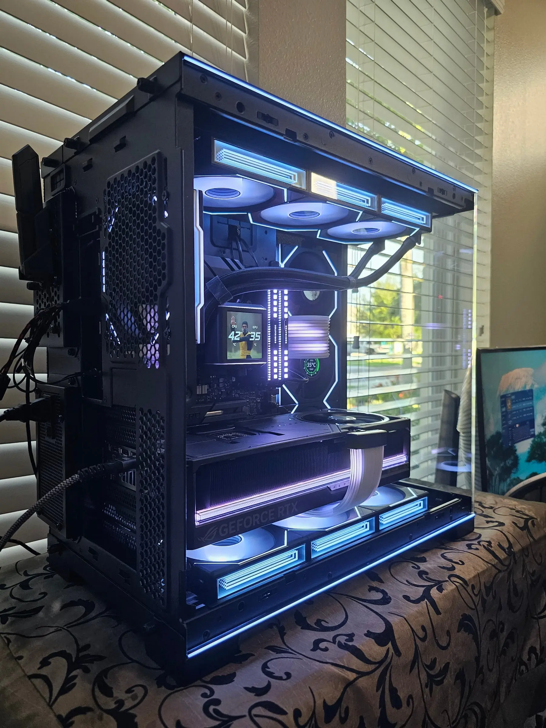Ice-blue interior — Galahad II LCD showing CPU and GPU temps over the Astral RTX 5090 and white Strimer runs