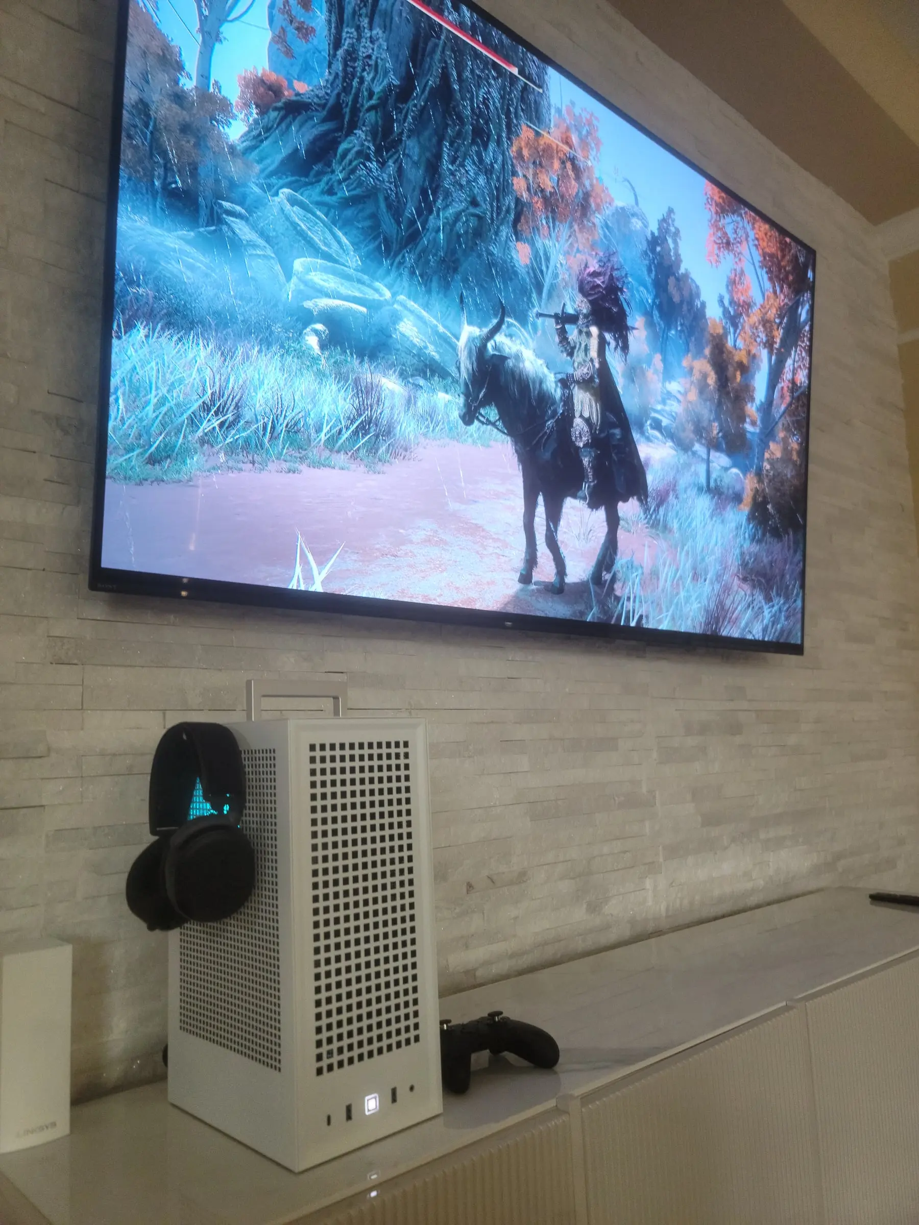 The Revolt 3 living its life — under a wall-mounted TV running Elden Ring, controller beside it, headset on the side hanger