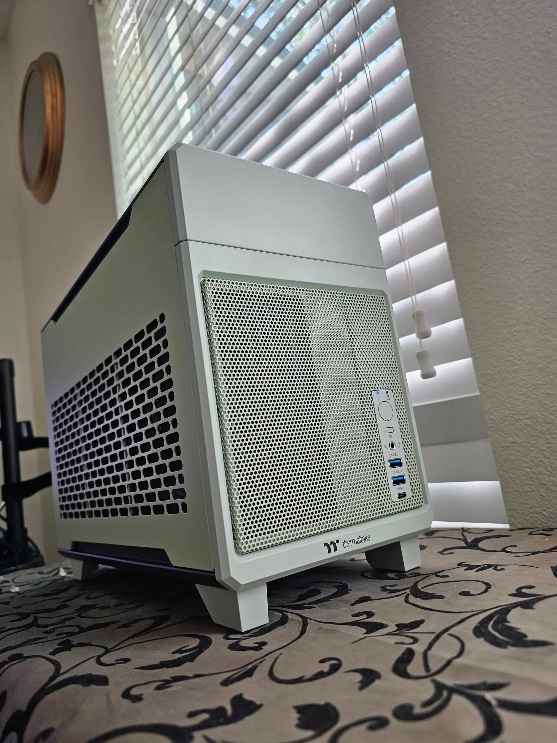 Thermaltake TR100 in matcha green, front-right corner view showing the Thermaltake logo and front I/O — power button, headphone jack, two USB 3.0 ports, and USB-C