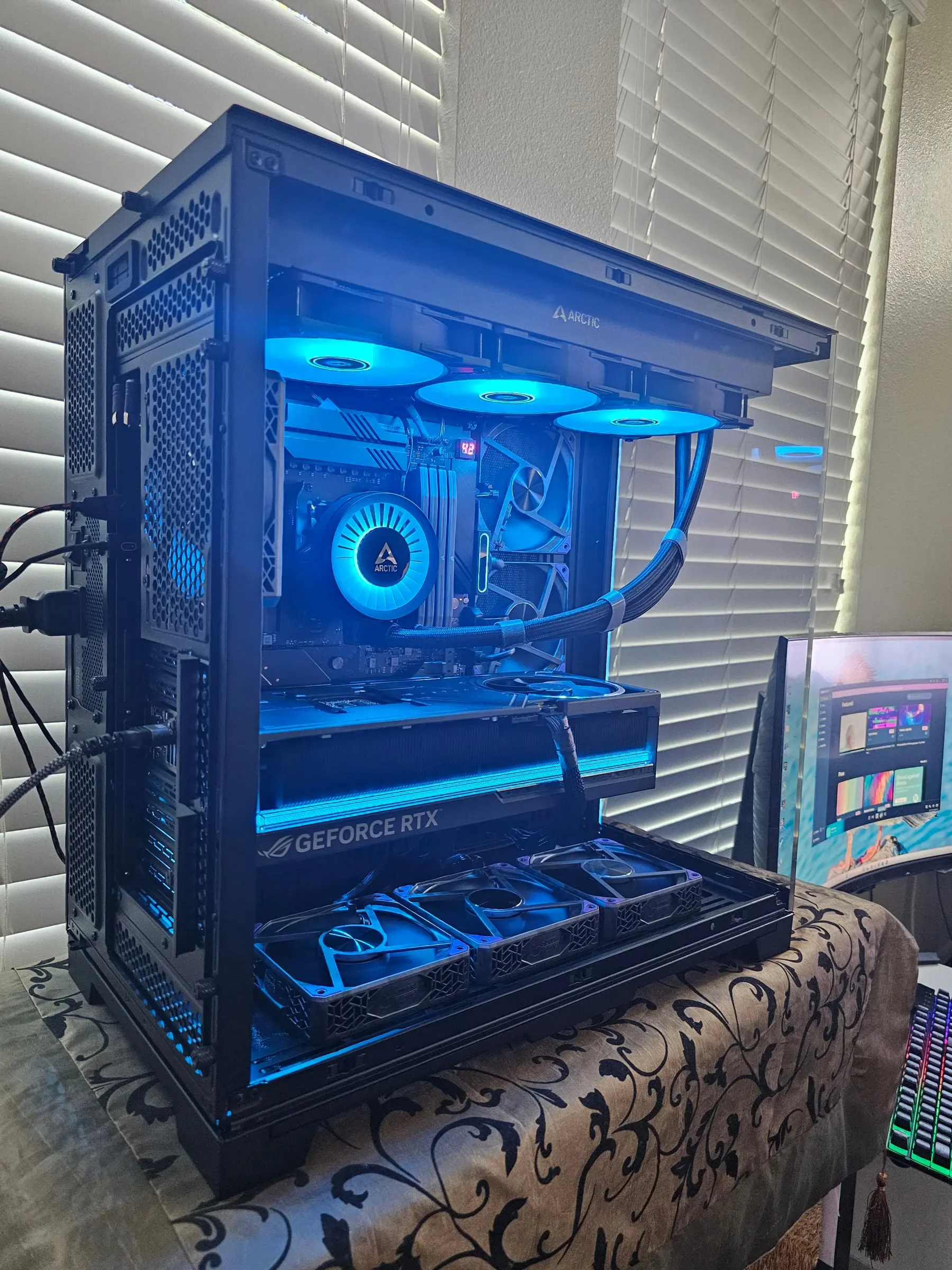 Blue theme with the Arctic pump logo lit and the ROG GeForce RTX badge glowing above the bottom fan trio